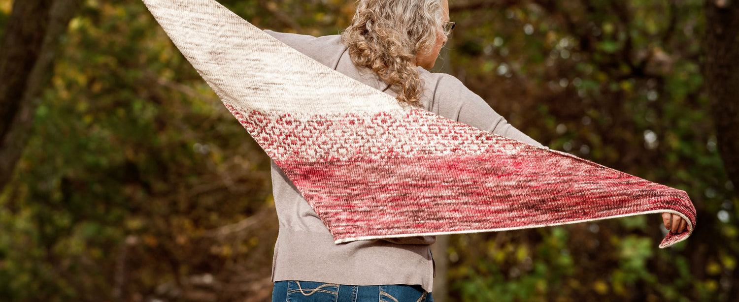 Woman wearing Cold Pale Moon hand knit shawl in Red Door Fibers hand-dyed yarn, standing outdoors with trees in the background